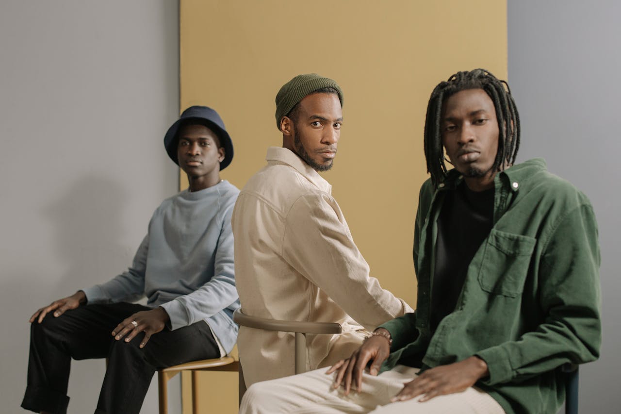 Three stylish men sitting in a minimalist studio with neutral tones and fashionable outfits.